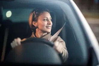 Frau mit Sicherheitsgurt lächelt, während sie ein Auto fährt.