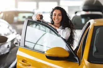 Lächende Frau öffnet die Fahrertür eines gelben Autos im Autohaus.